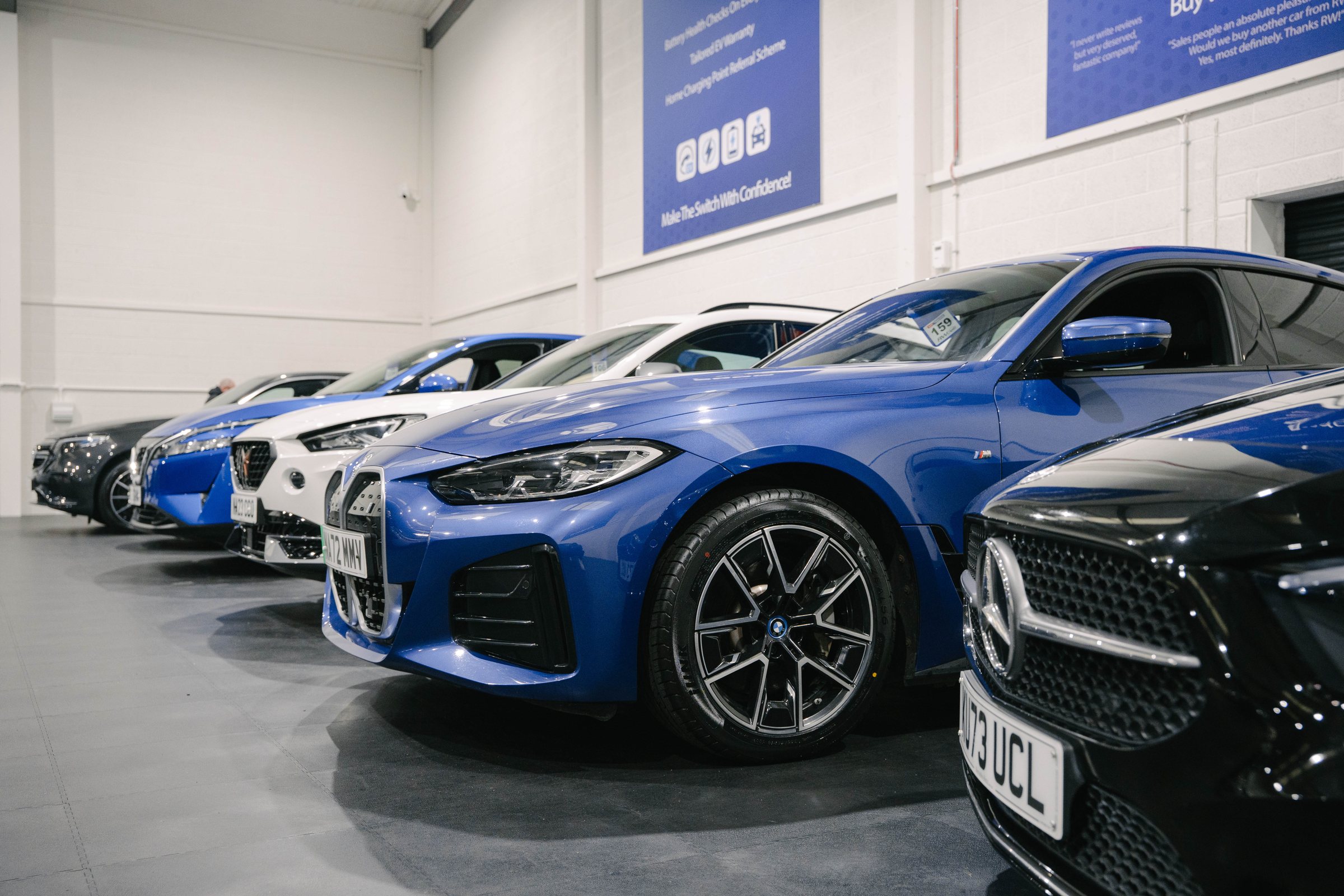 A line of cars in the RW Cars showroom with a blue BMW i4 at the front