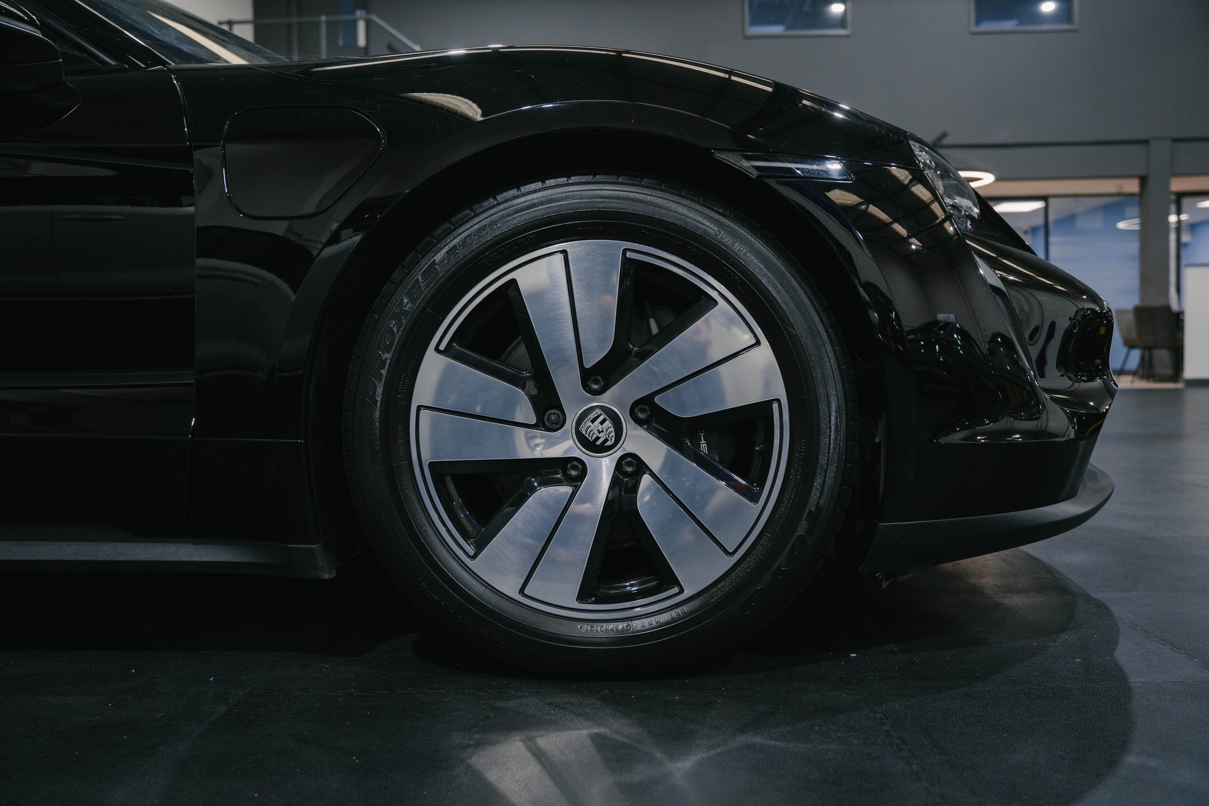 Close-up of a black Porsche Taycan's front wheel in the RW Cars showroom